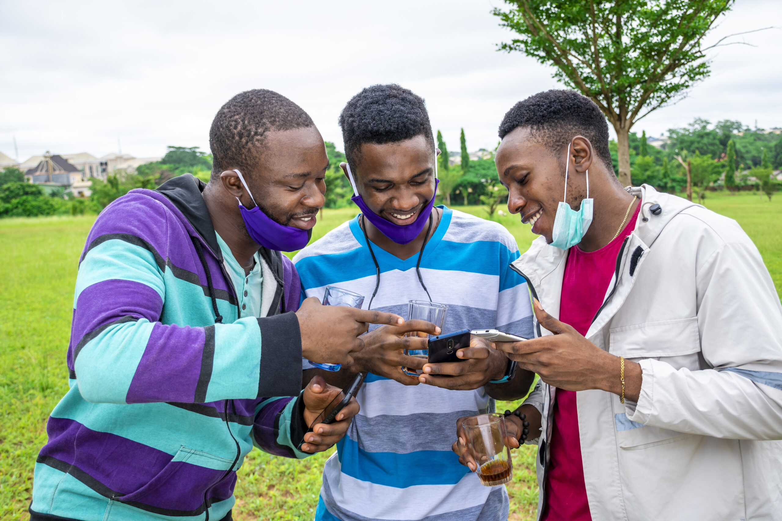 Groupe d'amis africains avec masques, boisson et téléphones, dans un parc