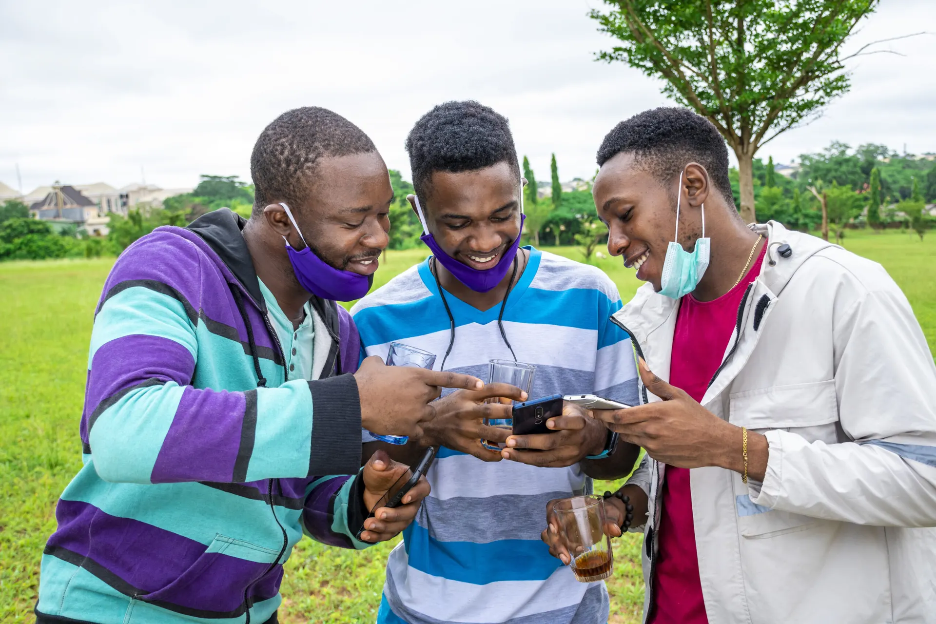 Groupe d'amis africains avec masques, boisson et téléphones, dans un parc